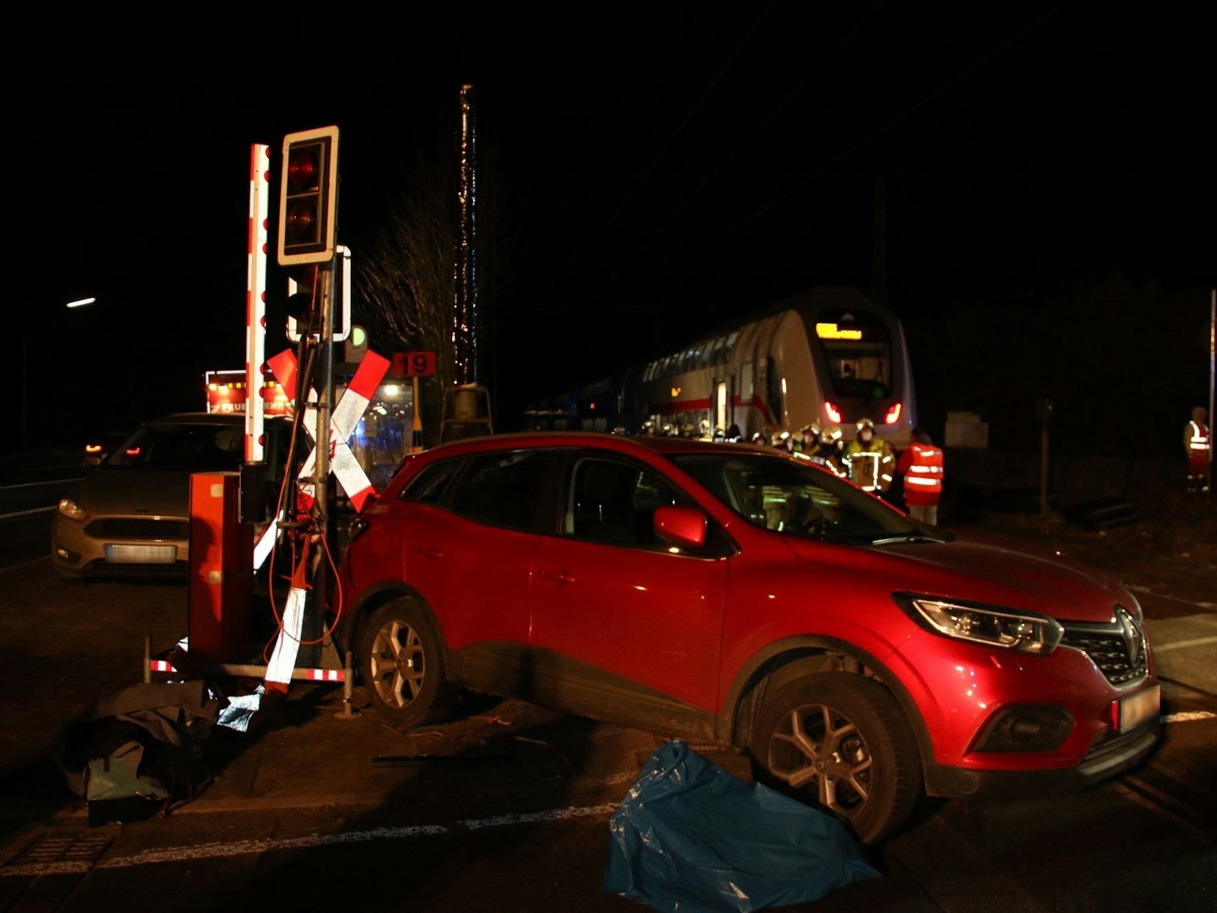 Ein Auto steht neben einer Schrankenanlage, im Hintergrund der ICE