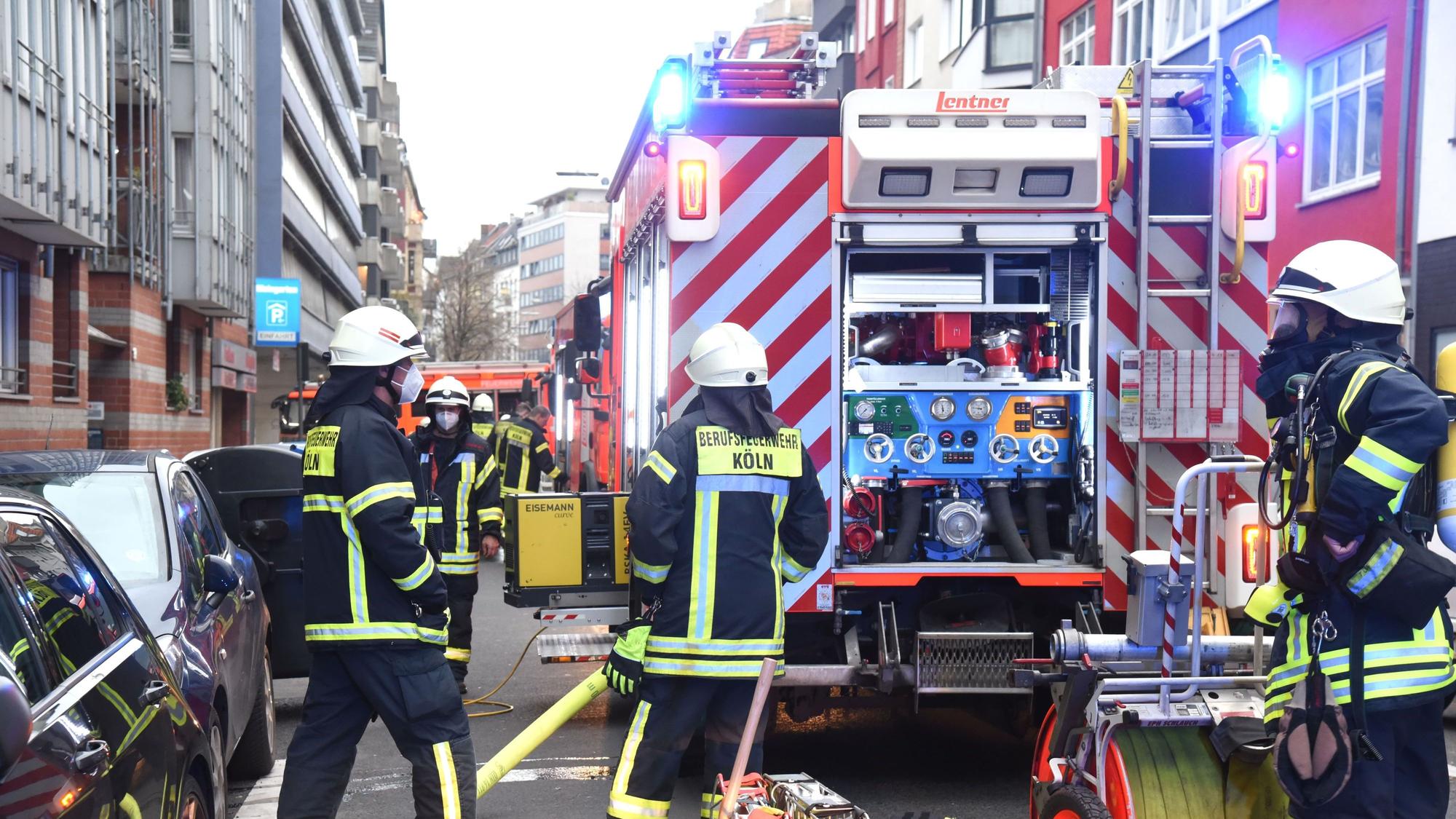 Drei Beamte der Feuerwehr stehen vor einem Einsatzwagen.