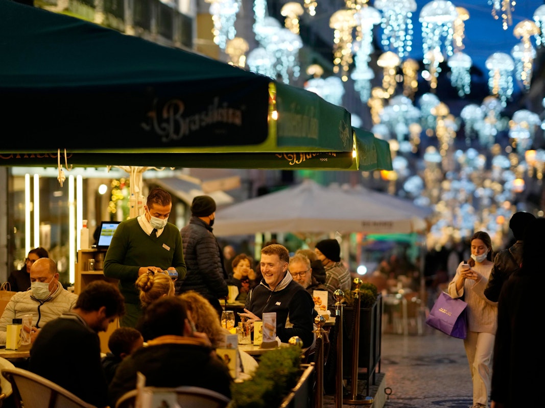 Menschen sitzen am 22. Dezember auf der Terrasse eines Cafés im weihnachtlich geschmückten Lissabonner Stadtteil Chiado. Nicht nur Portugal, auch Spanien und die USA werden Corona-Hochrisikogebiete.