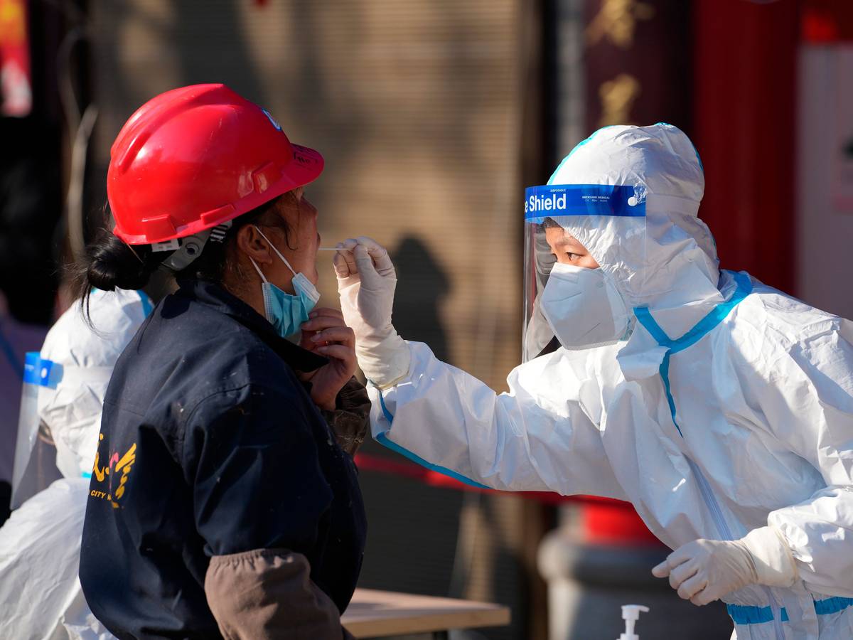 China, Xi'an: Eine Mitarbeiterin in einem medizinischen Schutzanzug entnimmt einer Frau an einer Corona-Teststation in der Provinz Shaanxi einen Abstrich über den Mund.