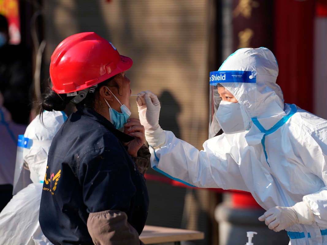 China, Xi'an: Eine Mitarbeiterin in einem medizinischen Schutzanzug entnimmt einer Frau an einer Corona-Teststation in der Provinz Shaanxi einen Abstrich über den Mund.