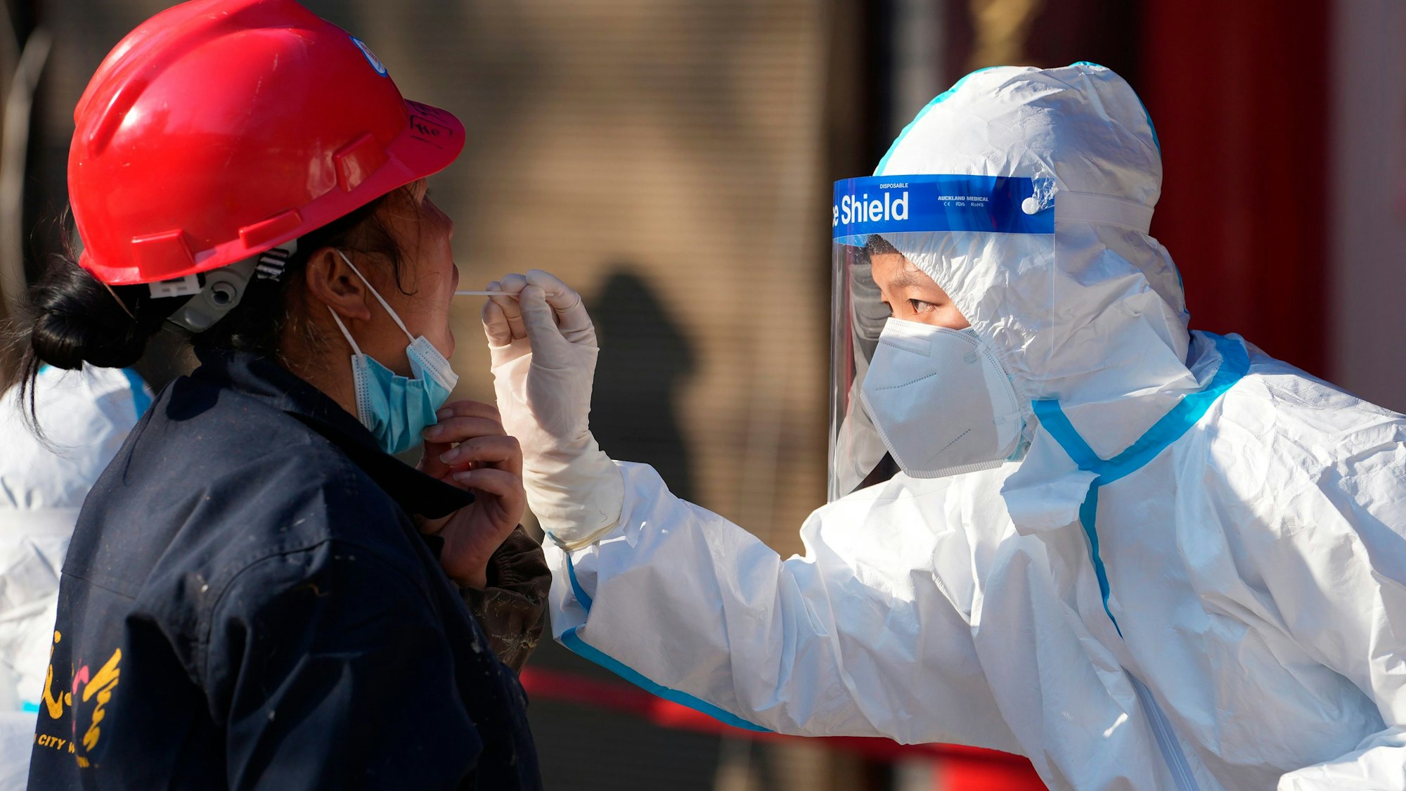 China, Xi'an: Eine Mitarbeiterin in einem medizinischen Schutzanzug entnimmt einer Frau an einer Corona-Teststation in der Provinz Shaanxi einen Abstrich über den Mund.