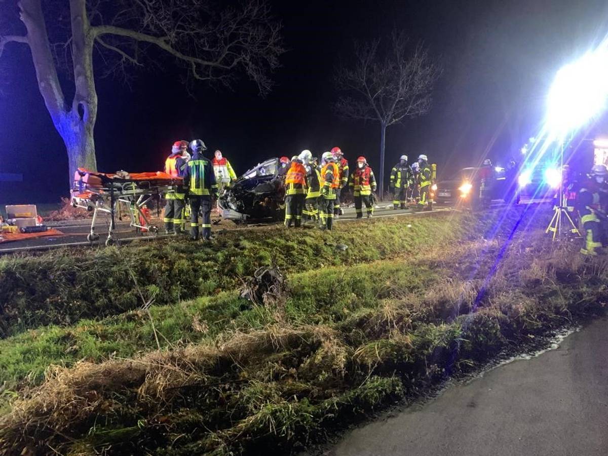 Einsatzkräfte der Feuerwehr stehen am Wrack auf der Straße.