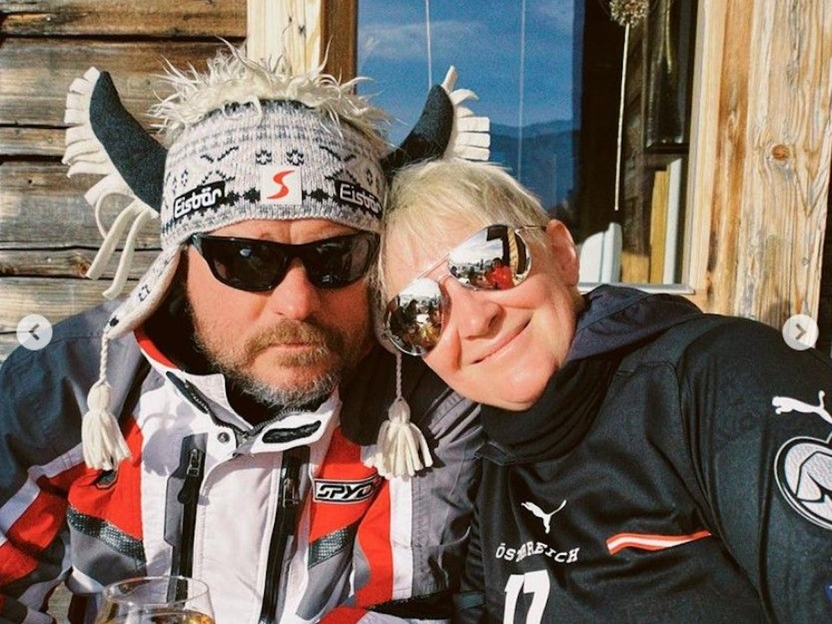 Steffen Baumgart sitzt mit seiner Frau Katja, Sonnenbrille und Hörner-Mütze an einer Skihütte in Österreich.