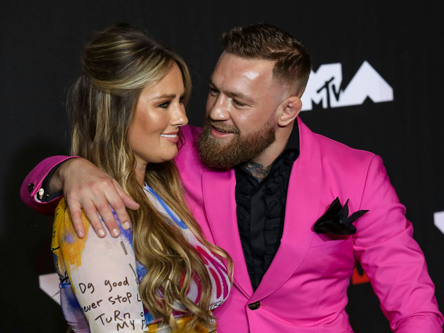 Conor McGregor trägt einen pinken Anzug und nimmt Dee Devlin in den Arm.