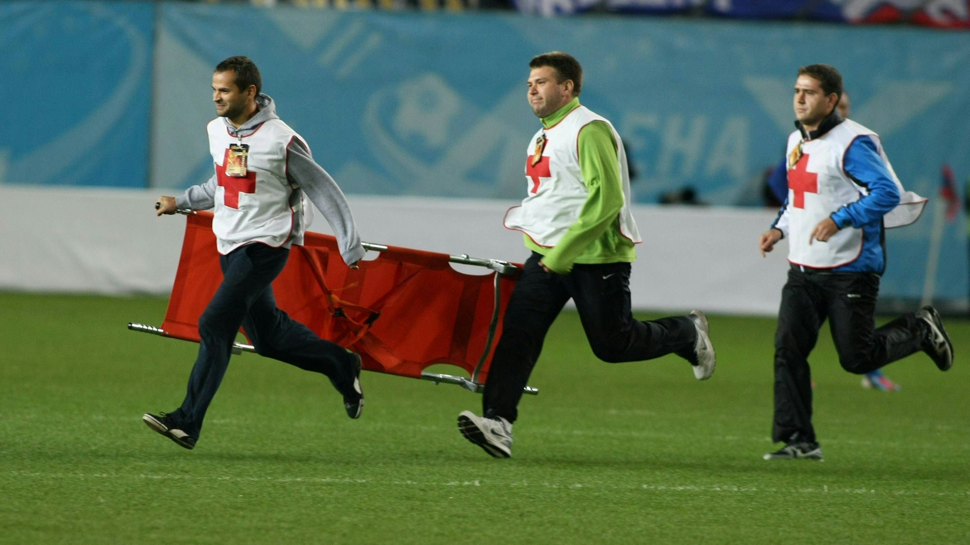 Drei Sanitäter rennen auf das Spielfeld. Sie haben eine Trage dabei.