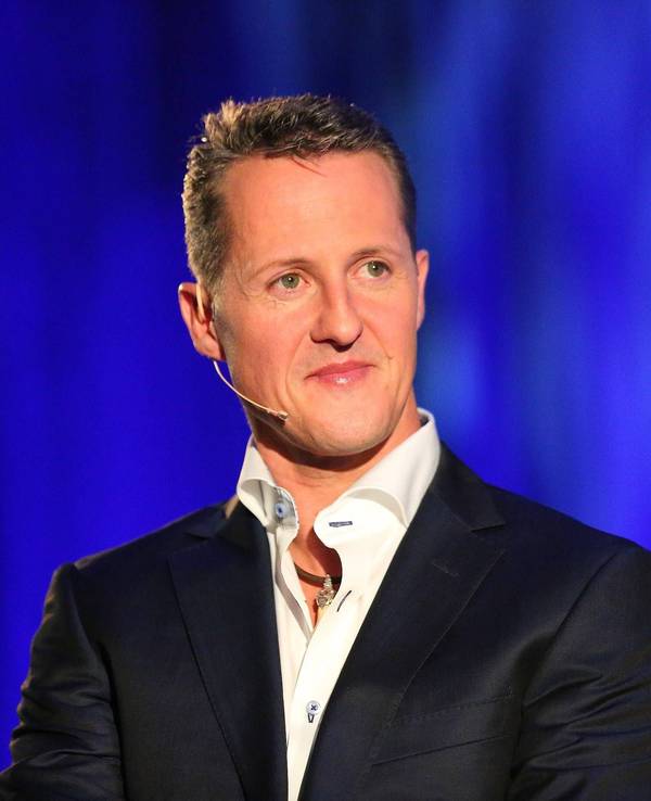Michael Schumacher sitzt auf einem Stuhl. Er trägt Hemd und Anzug.