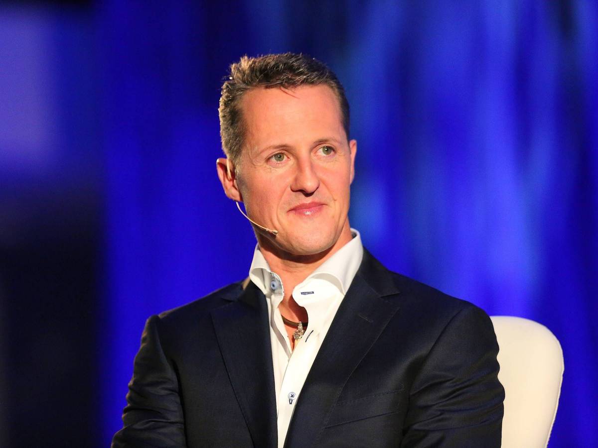 Michael Schumacher sitzt auf einem Stuhl. Er trägt Hemd und Anzug.