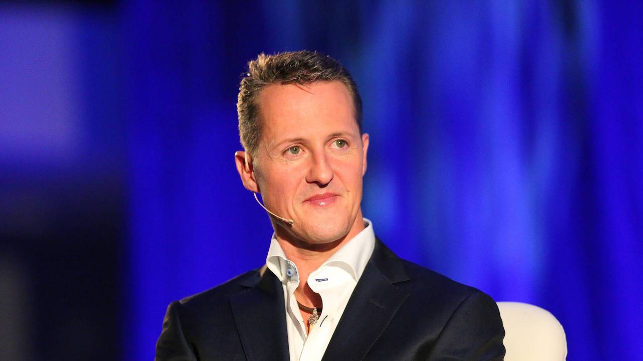 Michael Schumacher sitzt auf einem Stuhl. Er trägt Hemd und Anzug.