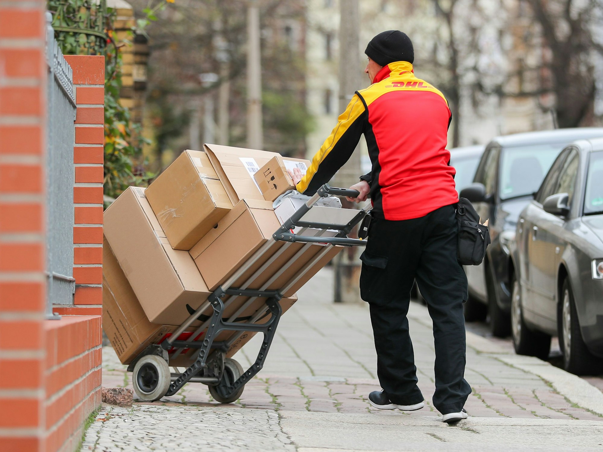 Das Symbolfoto aus dem Jahr 2019 zeigt einen DHL-Paketzusteller mit einer Sackkarre voller Pakete.