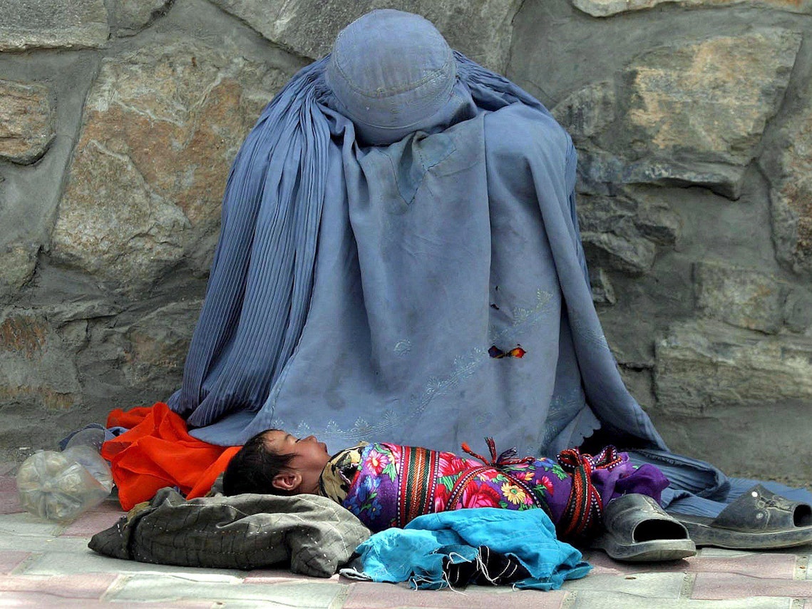 Eine Afghanin bettelt am Straßenrand um Almosen, ihr Säugling liegt vor ihr.