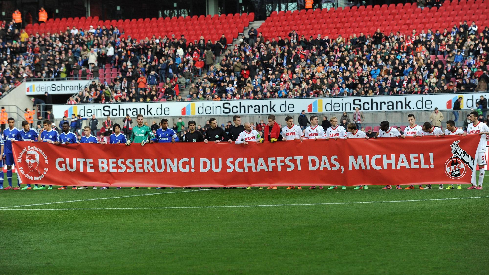Die Spieler des 1. FC Köln und die des FC Schalke halten ein Transparent vor Spielbeginn hoch, mit dem sie Michael Schumacher eine gute Genesung wünschen.