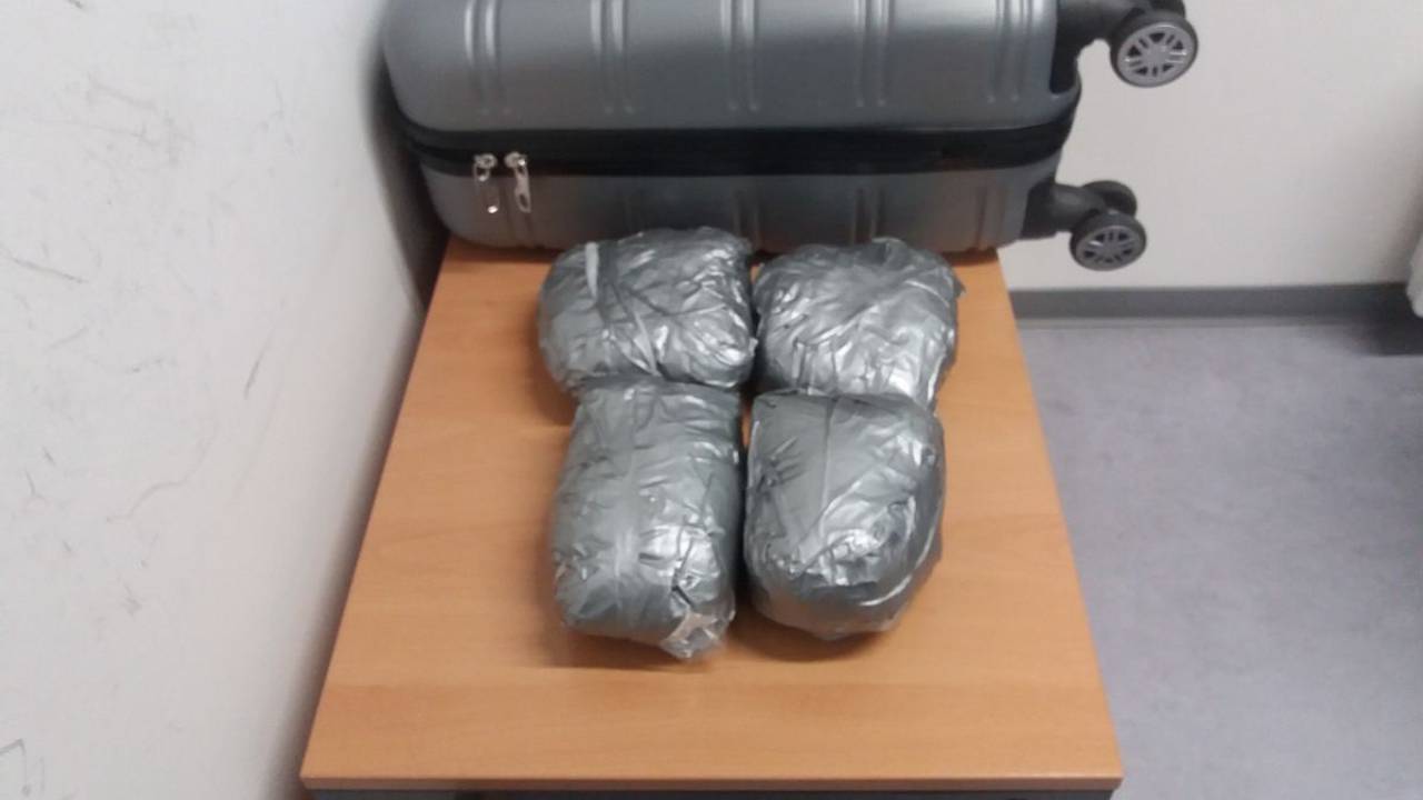 Vier Päckchen mit Drogen liegen vor einem Koffer auf einem Tisch.