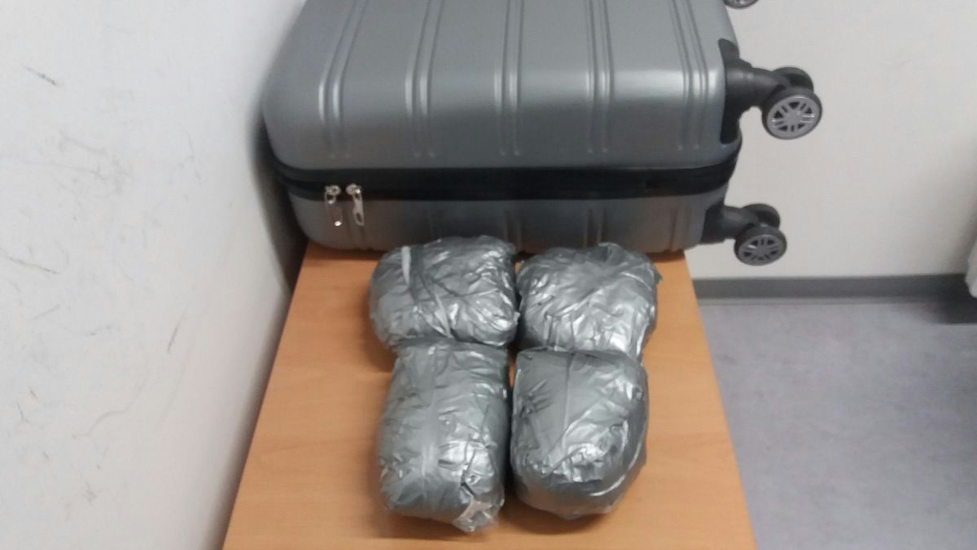 Vier Päckchen mit Drogen liegen vor einem Koffer auf einem Tisch.
