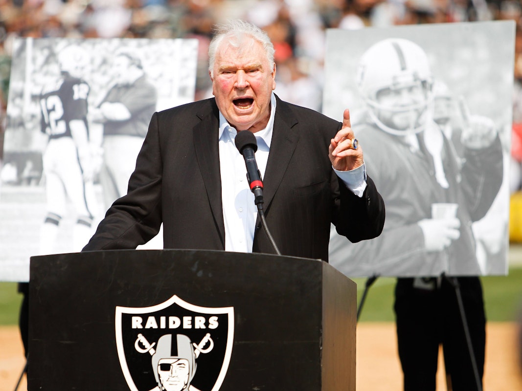 John Madden steht auf einem kleinen Podest, auf dem das Wappen der Las Vegas Raiders abgebildet ist.