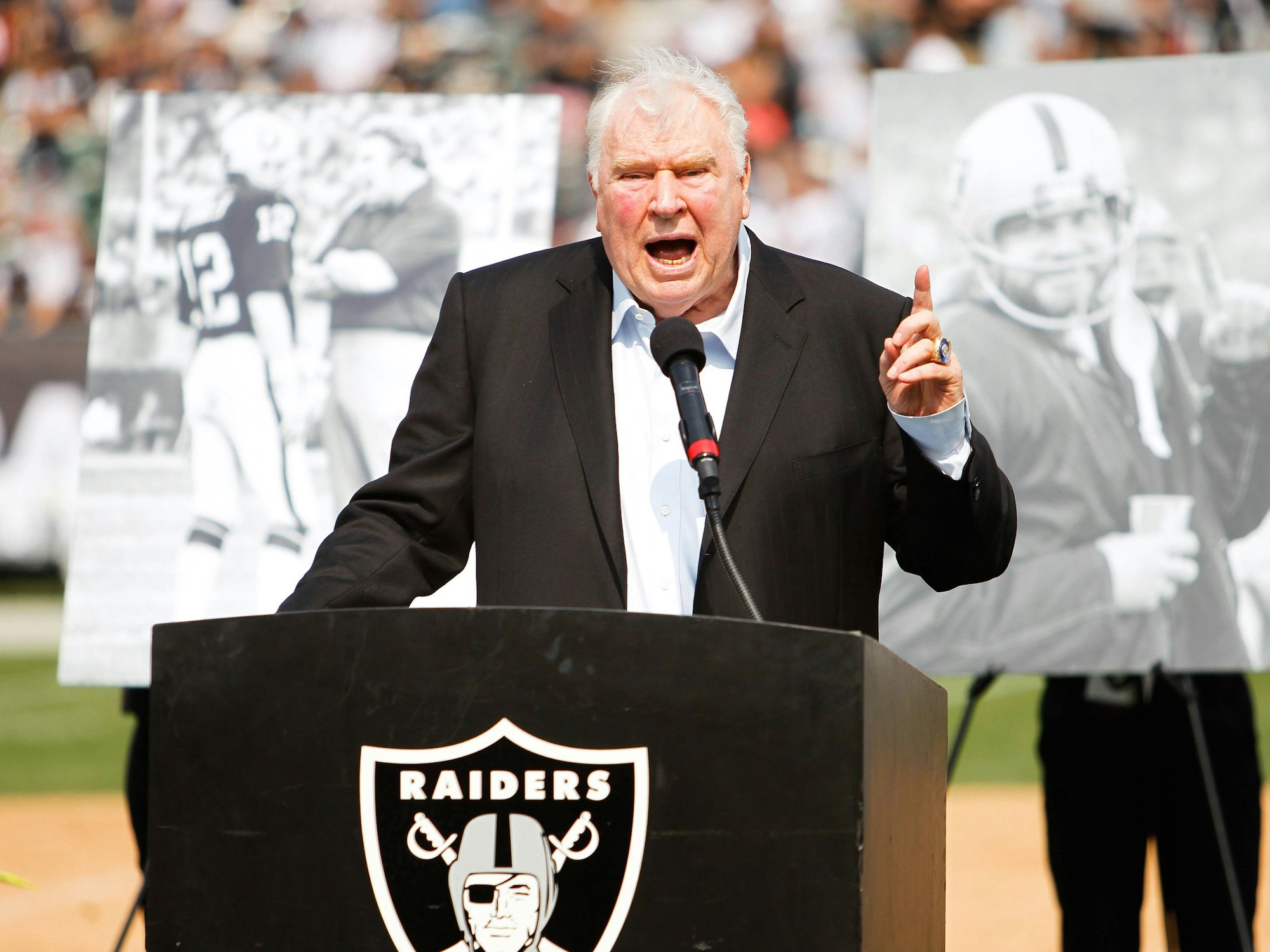 John Madden steht auf einem kleinen Podest, auf dem das Wappen der Las Vegas Raiders abgebildet ist.