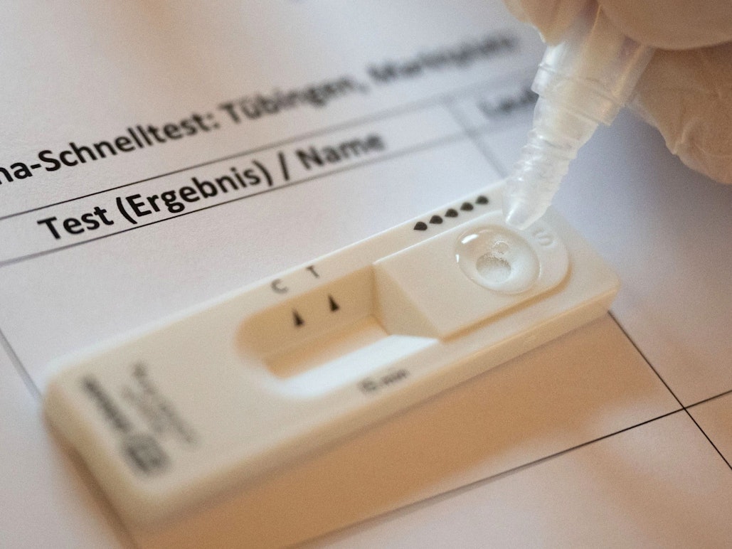 Ein Mitarbeiter einer Corona-Teststation träufelt Sekretlösung in die Kartusche eines Schnelltests.