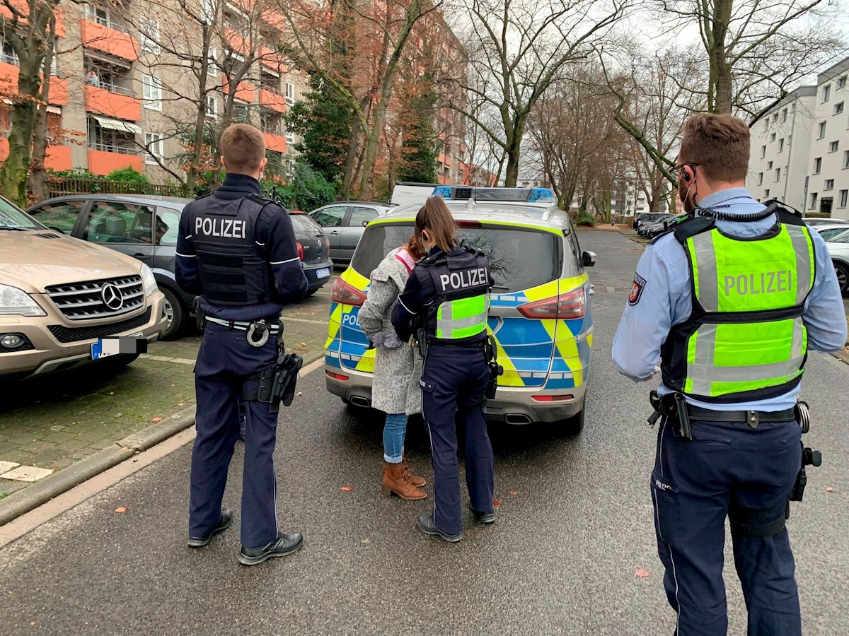 Eine Polizistin nimmt eine Frau fest, zwei Polizisten stehen daneben.