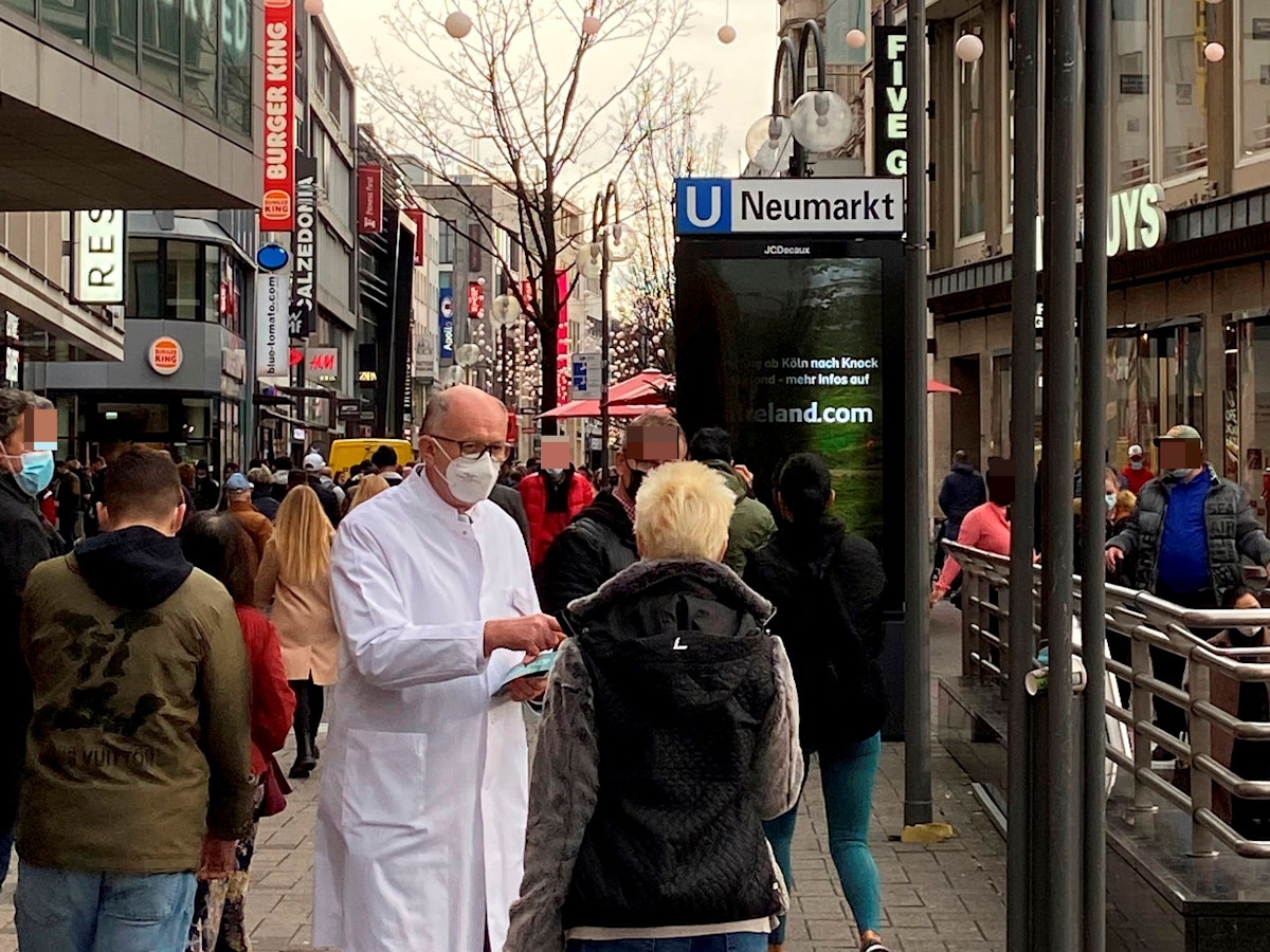 Gunther Quinkler steht im weißen Kittel in der Schildergasse und spricht mit einer Passantin.