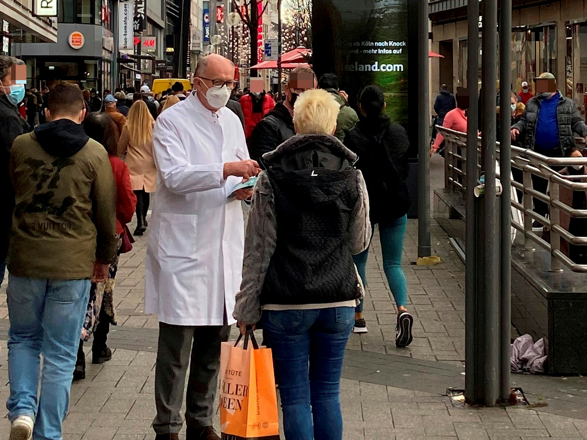 Gunther Quinkler steht im weißen Kittel in der Schildergasse und spricht mit einer Passantin.
