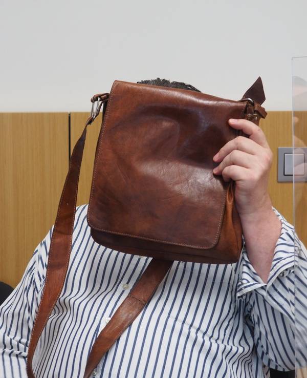 Hinter einer braunen Herren-Schultertasche verbirgt der angeklagte Betrüger im Düsseldorfer Gerichtssaal sein Gesicht.