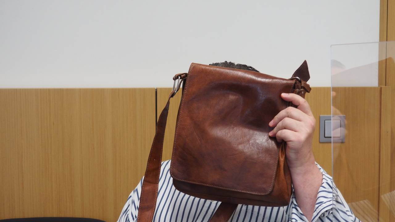 Hinter einer braunen Herren-Schultertasche verbirgt der angeklagte Betrüger im Düsseldorfer Gerichtssaal sein Gesicht.