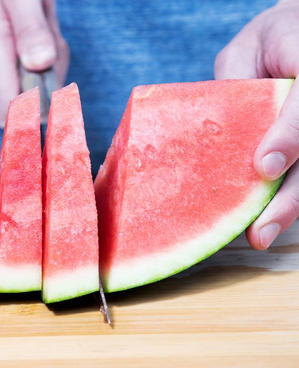 Ein Mann schneidet eine Wassermelone auf. Auch das Melonengrün – die weiße Schicht – kann man mitessen.