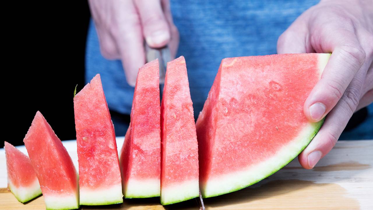 Ein Mann schneidet eine Wassermelone auf. Auch das Melonengrün – die weiße Schicht – kann man mitessen.