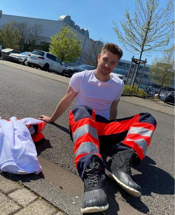 Dominik Flade sitzt in Arbeitskleidung eines Notfallsanitäters auf der Straße.