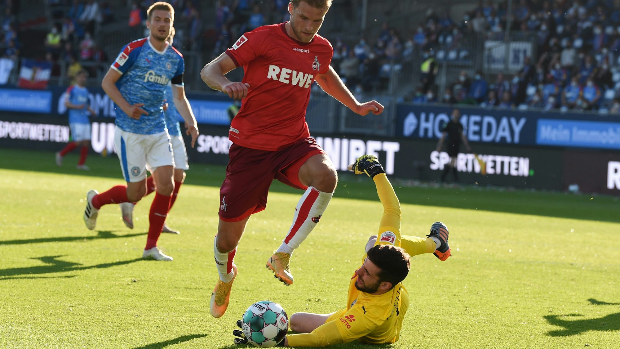 Sebastian Andersson (1. FC Köln) springt über Kiel-Keeper Ioannis Gelios.