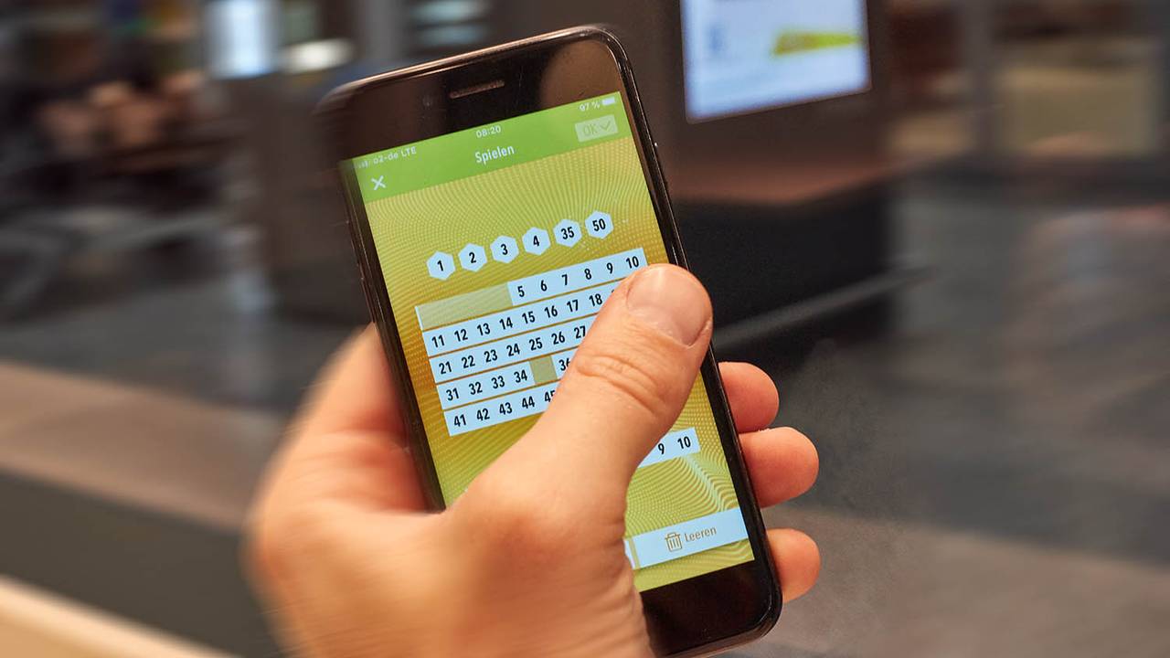 Hand hält Smartphone, auf dem Zahlen für Eurojackpot getippt werden. Eurojackpot Westlotto Smartphone