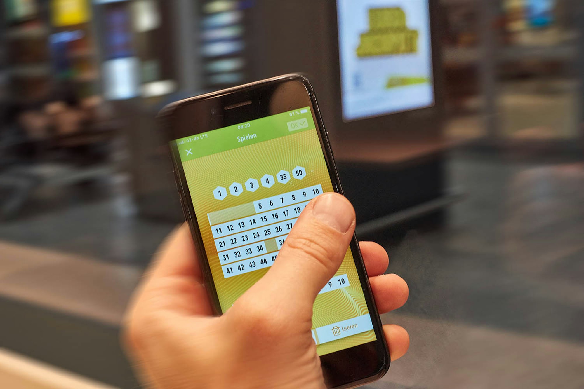 Hand hält Smartphone, auf dem Zahlen für Eurojackpot getippt werden. Eurojackpot Westlotto Smartphone