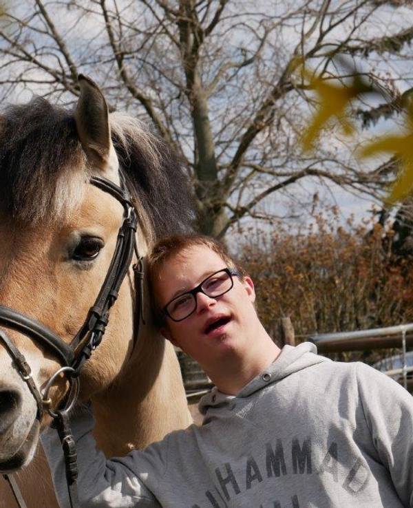 Ein junger Klient des Zentrums für therapeutisches Reiten in Köln Porz steht neben einem Therapiepferd.