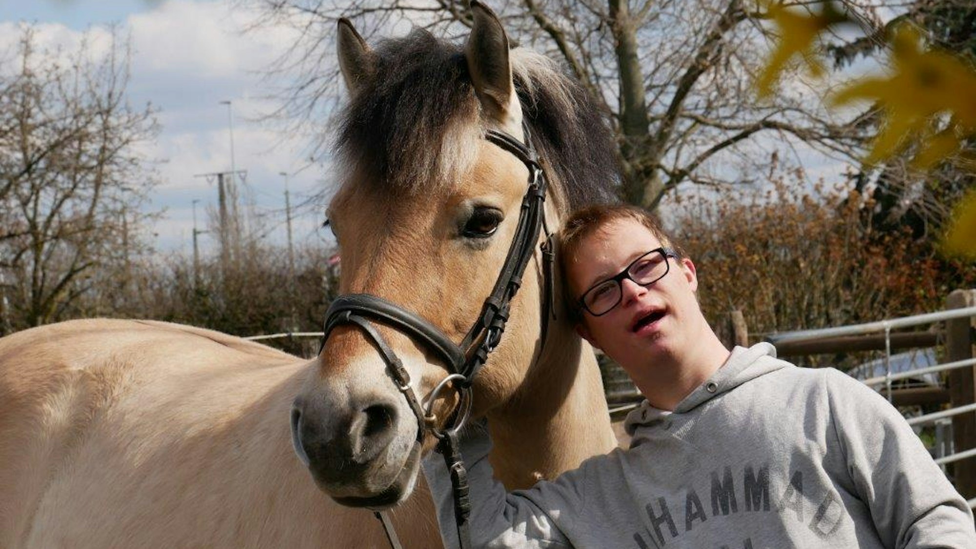 Ein junger Klient des Zentrums für therapeutisches Reiten in Köln Porz steht neben einem Therapiepferd.