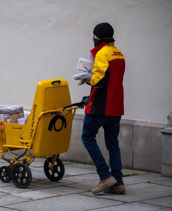 Ein DHL-Bote verteilt mit Mund-Nasen-Schutz Briefe.