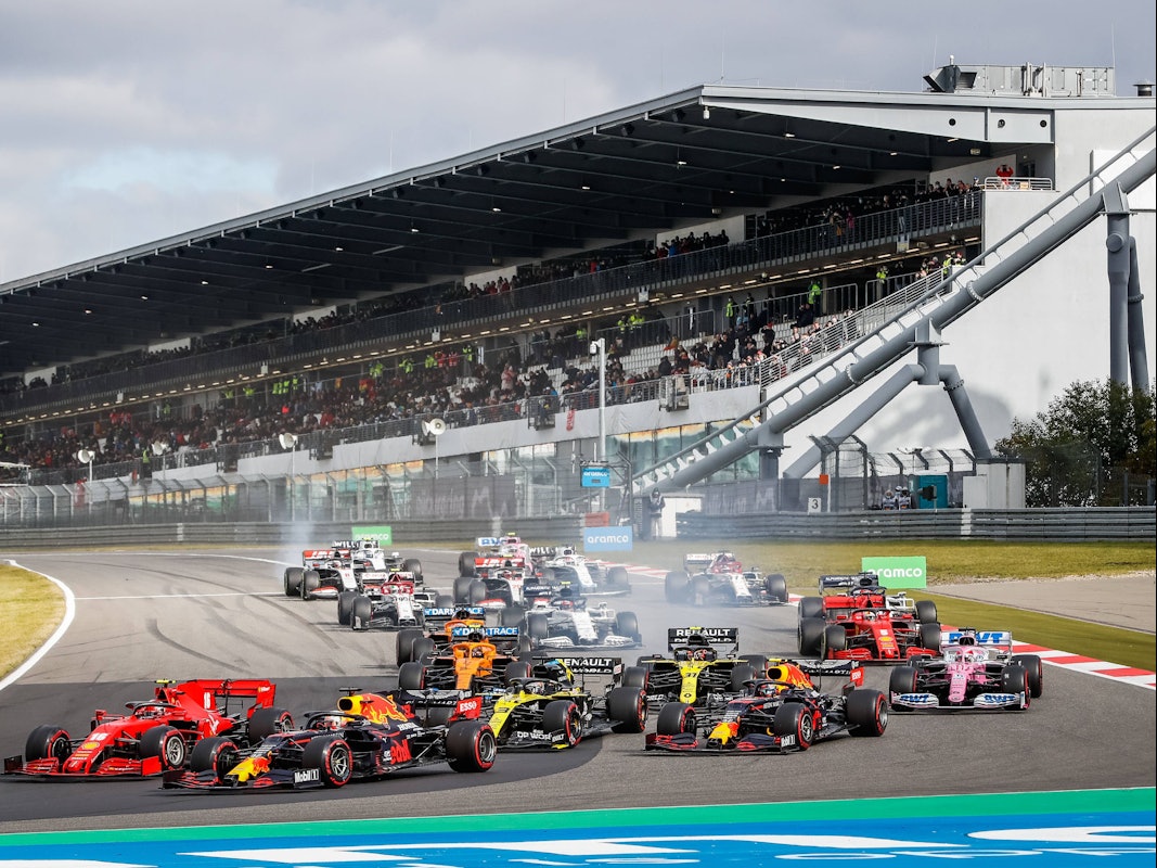 Max Verstappen fährt mit seinem Red Bull an der Spitze. Die Rennwagen der anderen Fahrer sind allesamt knapp dahinter. Im Hintergrund ist die Tribüne zu sehen.