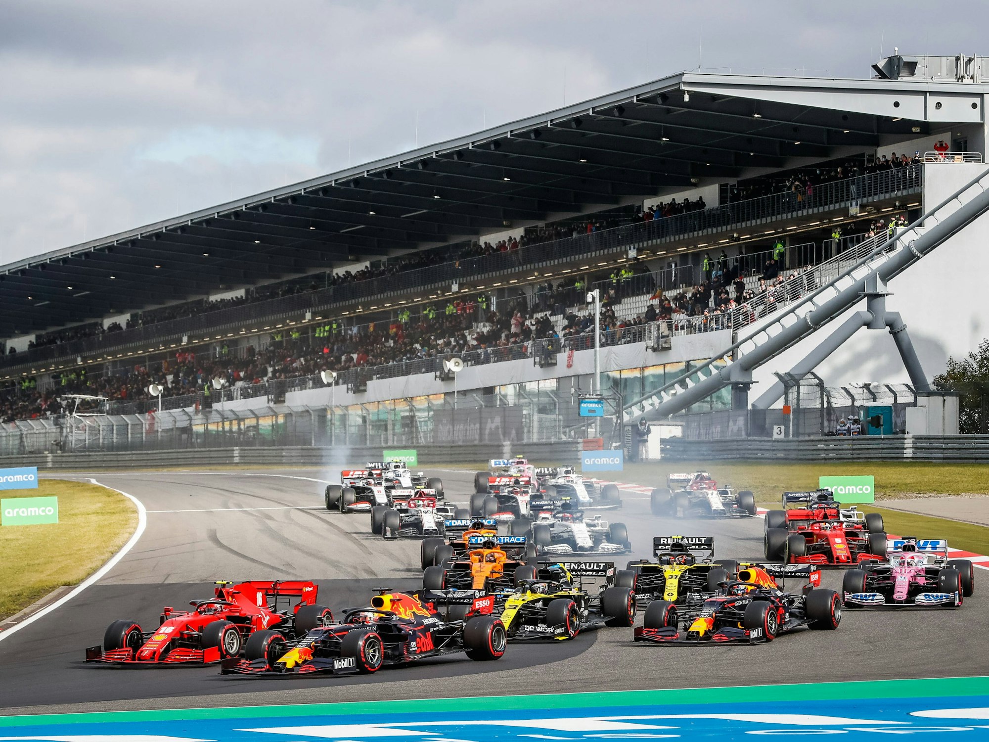 Max Verstappen fährt mit seinem Red Bull an der Spitze. Die Rennwagen der anderen Fahrer sind allesamt knapp dahinter. Im Hintergrund ist die Tribüne zu sehen.