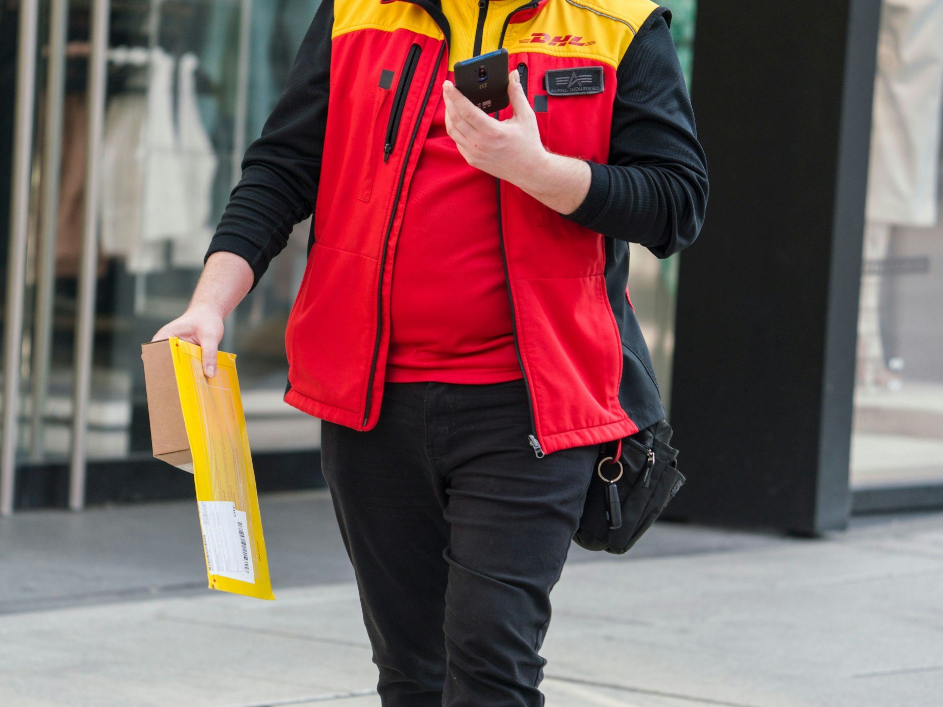 Unverrichteter Dinge geht ein DHL-Bote wieder zurück zu seinem Fahrzeug, nachdem er einen Brief und ein Päckchen nicht abliefern konnte. Das Symbolbild wurde im März 2020 in Frankfurt a.M. aufgenommen.