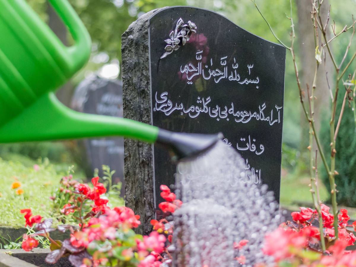Jemand gießt die Blumen auf einem muslimischen Grab.