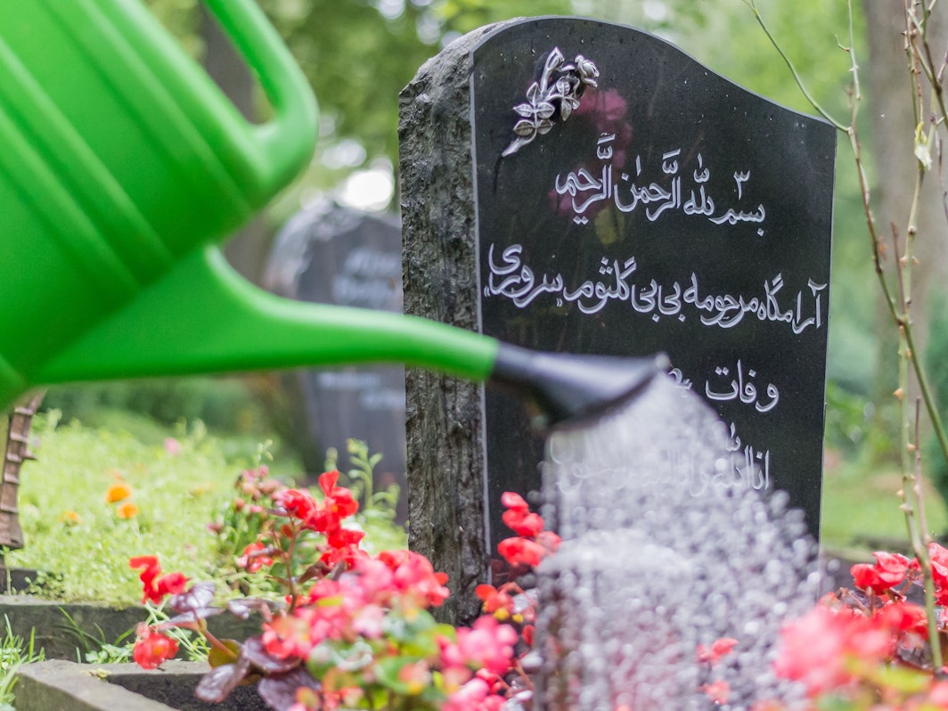 Jemand gießt die Blumen auf einem muslimischen Grab.
