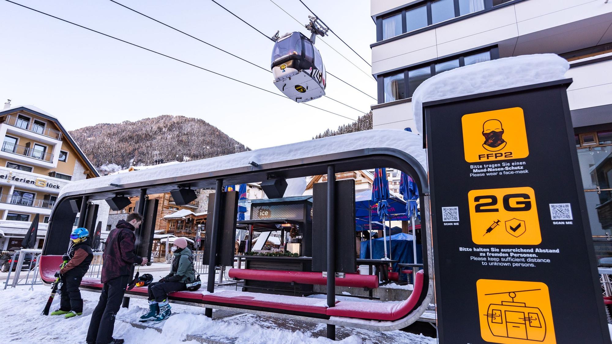 Skifahrer warten im Skigebiet bei der Gondel, wo Schilder auf die Corona-Regelungen hinweisen. +++ dpa-Bildfunk +++