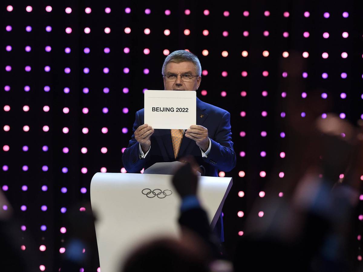 Thomas Bach hält ein Schild hoch, auf dem „Beijing 2022“ steht.