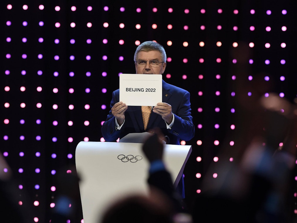 Thomas Bach hält ein Schild hoch, auf dem „Beijing 2022“ steht.