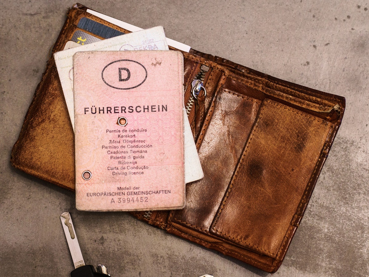 Ein rosa Führerschein, ein Autoschlüssel, eine Geldbörse und ein Fahrzeugschein liegen auf dem Tisch. Bis 2033 müssen Millionen von Führerscheinen umgetauscht werden, damit sie fälschungssicherer sind.