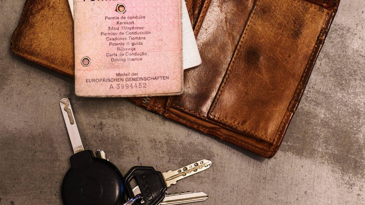 Ein rosa Führerschein, ein Autoschlüssel, eine Geldbörse und ein Fahrzeugschein liegen auf dem Tisch. Bis 2033 müssen Millionen von Führerscheinen umgetauscht werden, damit sie fälschungssicherer sind.