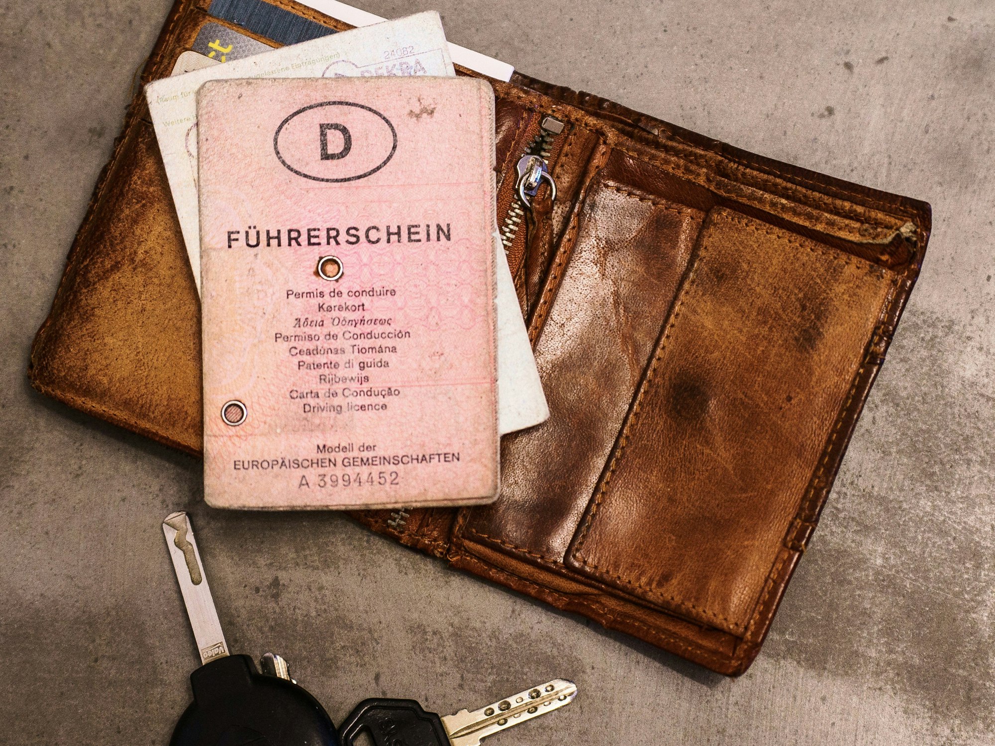 Ein rosa Führerschein, ein Autoschlüssel, eine Geldbörse und ein Fahrzeugschein liegen auf dem Tisch. Bis 2033 müssen Millionen von Führerscheinen umgetauscht werden, damit sie fälschungssicherer sind.