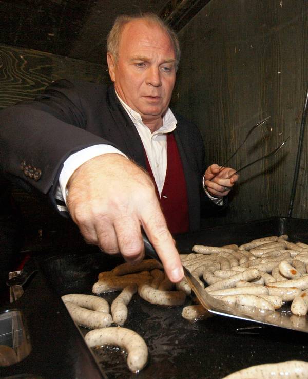 Uli Hoeneß wendet auf einem Grill kleine Nürnberger Würstchen.