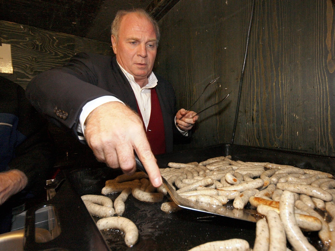 Uli Hoeneß wendet auf einem Grill kleine Nürnberger Würstchen.