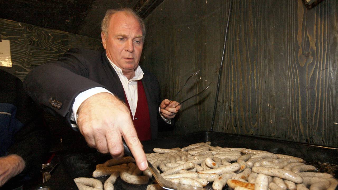 Uli Hoeneß wendet auf einem Grill kleine Nürnberger Würstchen.