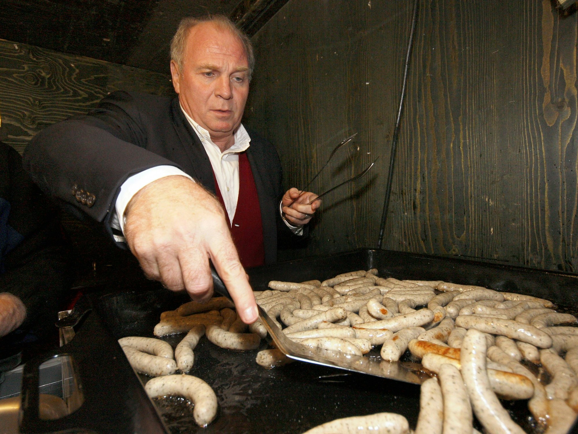 Uli Hoeneß wendet auf einem Grill kleine Nürnberger Würstchen.